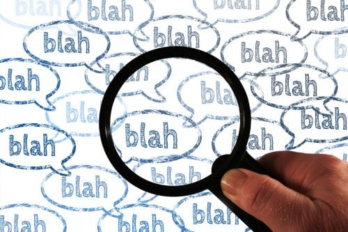 hand holding magnifying glass over speech bubbles containing the words 'blah blah blah'